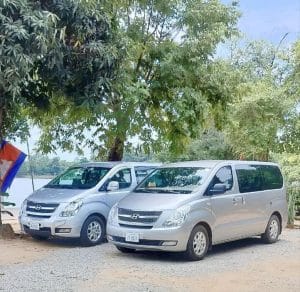 Two silver Hyundai H1 private transfer vans parked by a lake in Cambodia