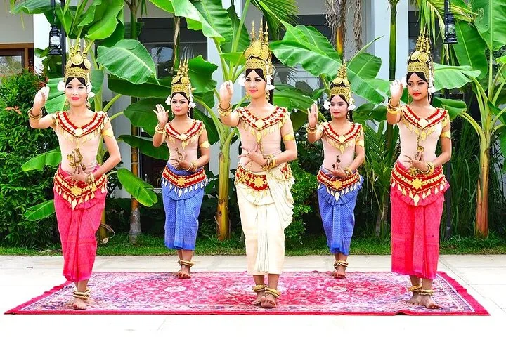 Five apsara dancers in gold headdresses and silk costumes perform on a red carpet in a garden in Siem Reap