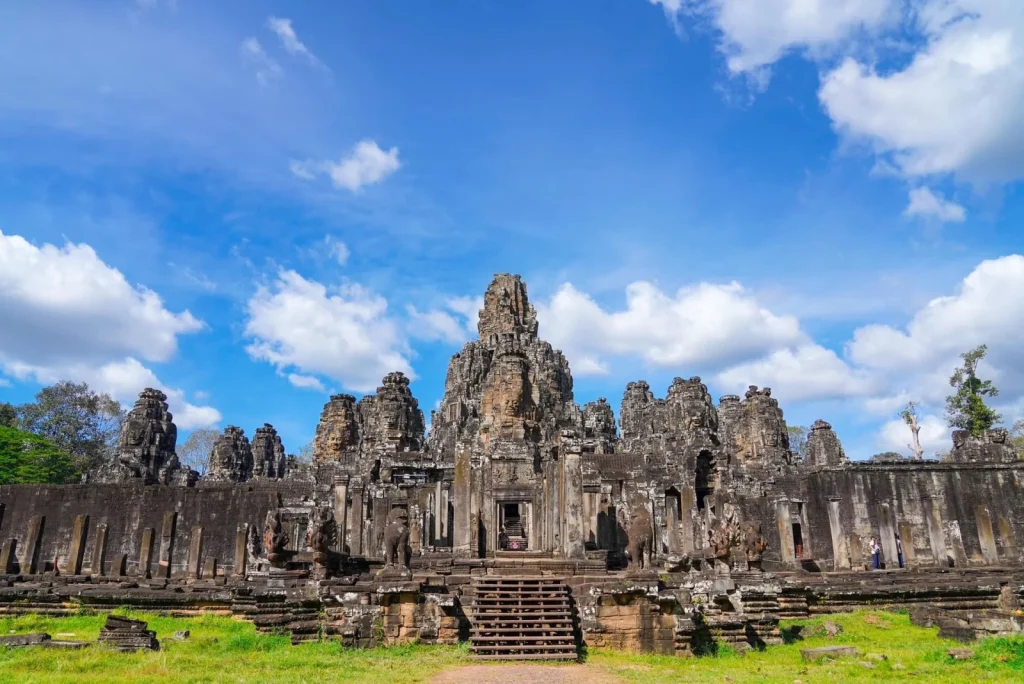 The full Bayon temple seen across grass under a bright cloudy sky